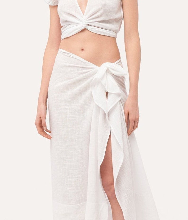 May include: A white cotton wrap skirt with a side slit and a knotted tie at the waist.