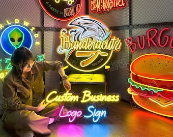 May include: A collection of custom neon signs for businesses. The signs feature various designs, including a food truck, a bear wearing sunglasses, a barber shop logo, a burger, and an alien. The signs are all lit up and have a bright, colorful glow.