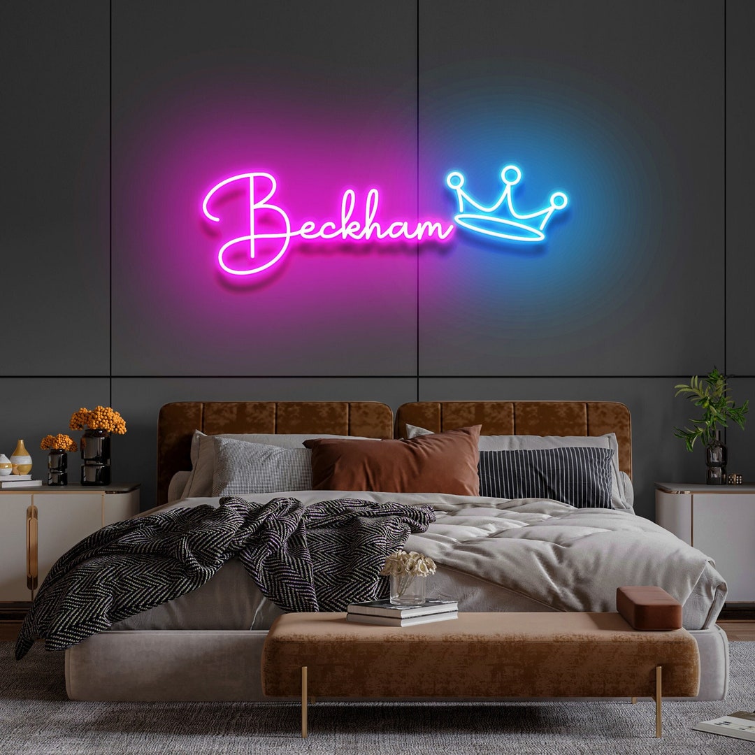 Personalized pink neon name sign with a blue crown above a bedroom bed