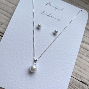May include: A silver necklace with a single pearl pendant and matching pearl stud earrings are displayed on a white card. The card has the words "Beautiful Bridesmaid" written in cursive script.