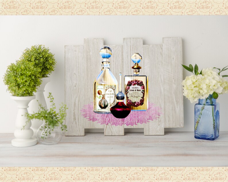 May include: Three glass bottles of perfume with decorative labels and stoppers, displayed on a wooden shelf with a pink lace overlay. The bottles are arranged in a row, with the largest bottle in the center. The bottles are surrounded by white flowers and green plants.