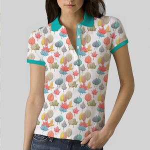 May include: A white polo shirt with a teal collar and trim. The shirt features a colourful leaf pattern.