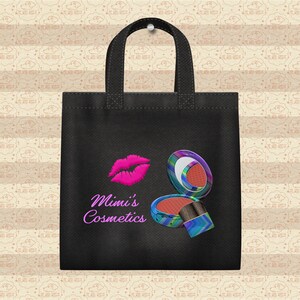Peut inclure: Sac fourre-tout noir avec un imprim&eacute; de l&egrave;vres roses et un design de compact de maquillage color&eacute;. Le texte "Mimi's Cosmetics" est imprim&eacute; sur le sac.