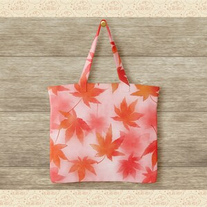 May include: A pink tote bag with a watercolour design of red maple leaves. The bag is hanging on a wooden wall.