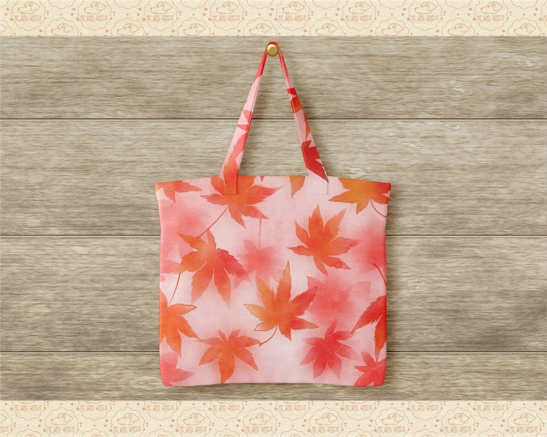 May include: A pink tote bag with a watercolour design of red maple leaves. The bag is hanging on a wooden wall.