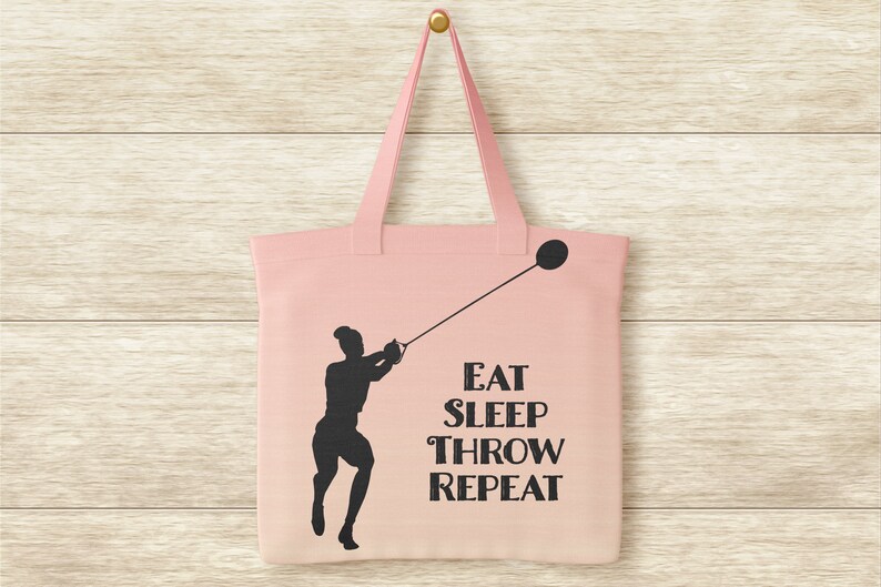 Pu&ograve; includere: Una borsa di tela rosa con la silhouette di una persona che lancia un martello. Il testo sulla borsa dice "Eat Sleep Throw Repeat."