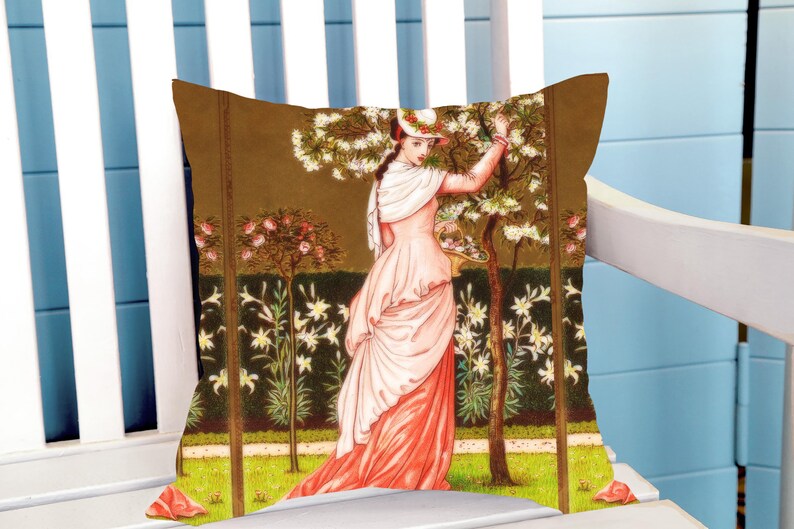 May include: Cushion with a vintage illustration of a woman in a pink dress in a garden. The cushion has a brown background with trees and flowers. The woman is reaching up to pick flowers.