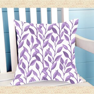 May include: A white cushion with a purple floral pattern. The cushion features a repeating pattern of stylised leaves and branches.