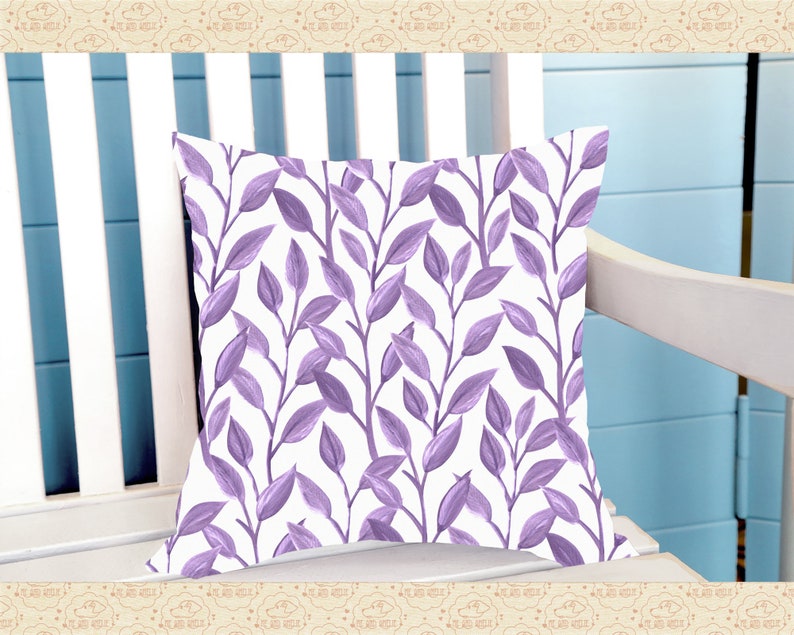 May include: A white cushion with a purple floral pattern. The cushion features a repeating pattern of stylised leaves and branches.