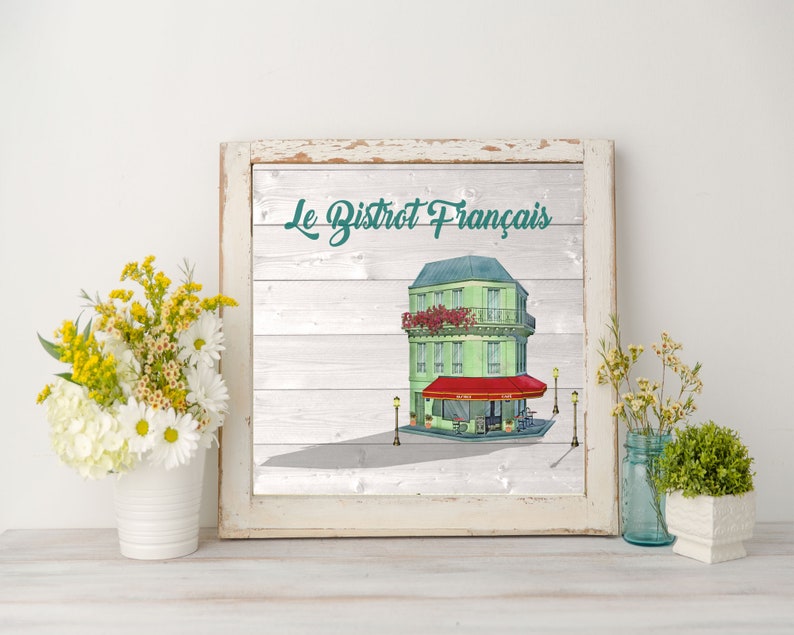 May include: A white framed print with a woodgrain background featuring a cartoon illustration of a green French bistro building with a red awning. The text "Le Bistrot Fran&ccedil;ais" is written in teal above the building.