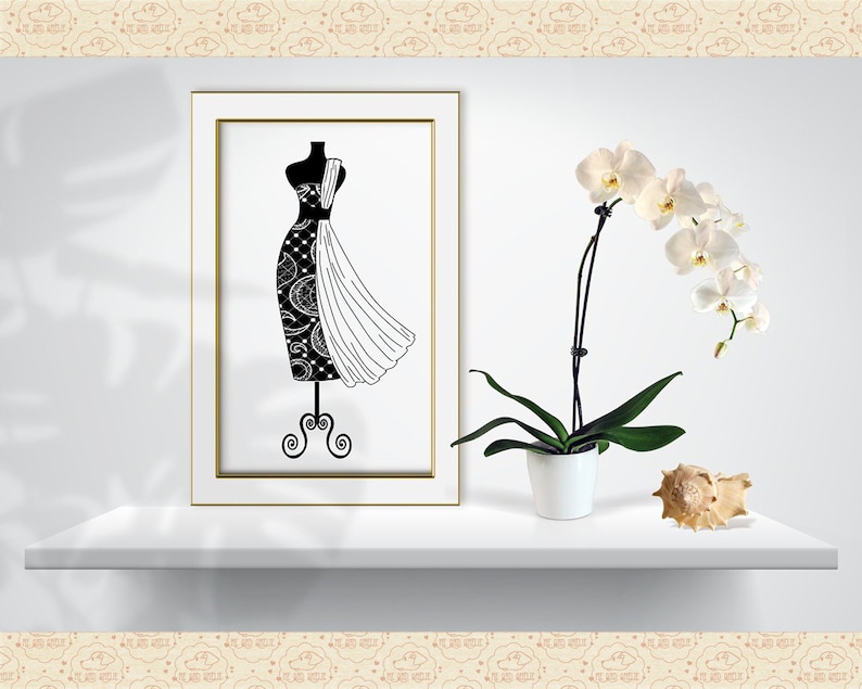Op de afbeelding: Een zwart-wit illustratie van een paspop met een patroonontwerp. Het kunstwerk wordt tentoongesteld op een witte plank, naast een orchidee in pot en een zeeschelp. De lijst heeft een gouden rand.