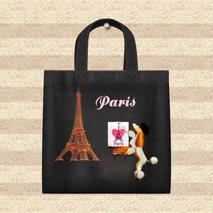May include: Black tote bag with a white Eiffel Tower, a pink heart, and a poodle painting a picture of the Eiffel Tower. The bag has the word "Paris" written in pink letters.