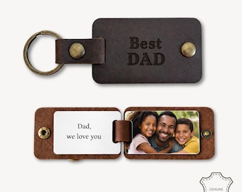 Op de afbeelding: Een donkerbruine leren sleutelhanger met een metalen ring en messingkleurige drukknopen. De voorzijde is gegraveerd met de tekst "Best DAD". Wanneer geopend, toont het een wit inzetstuk met de tekst "Dad, we love you" en een kleurenfoto van een man en twee kinderen.