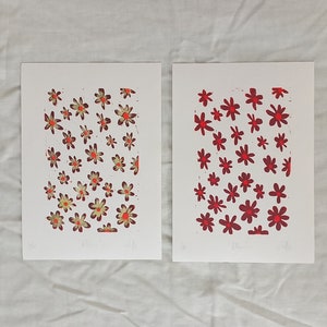 May include: Two floral art prints on white paper. One print features red and yellow flowers, the other showcases red flowers. Each print has the word "Willow" and artist's signature at the bottom. The prints are displayed on a white surface.