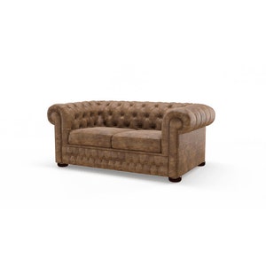 Pode incluir: Um sofá Chesterfield castanho de dois lugares com encosto e assento almofadados. Os braços enrolados são acentuados com tachas. O sofá tem um design clássico e vintage e está sobre um fundo branco.
