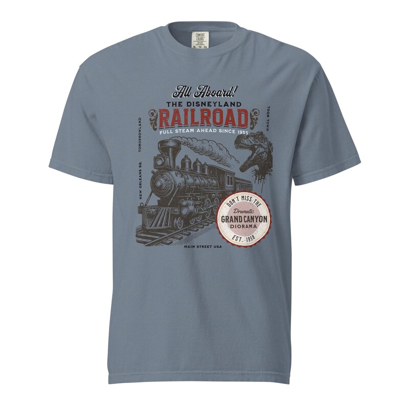 May include: A blue t-shirt featuring a vintage-style graphic of a steam train, with the text "All Aboard! The Disneyland Railroad" and "Don't Miss the Grand Canyon Diorama." The design includes a dinosaur silhouette.