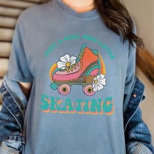 May include: A blue t-shirt with a retro graphic of a roller skate with flowers and the text "Just a girl who loves skating".