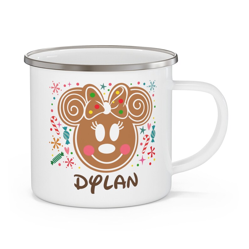May include: White enamel mug with a gingerbread Minnie Mouse design. The design includes a brown gingerbread face with a bow, pink cheeks, and the name "DYLAN" in brown text. Colorful candy and snowflake accents surround the character.