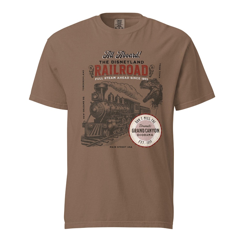 May include: Brown t-shirt featuring a vintage-style graphic of a steam train on tracks. The design includes the text "All Aboard! The Disneyland Railroad" and "Don't Miss the Grand Canyon Diorama Est. 1958."