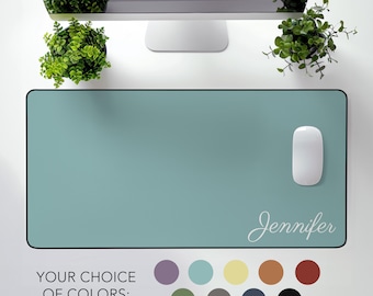 May include: A light blue desk mat with a black border and the name "Jennifer" written in white script. The mat is on a white surface with a computer monitor, a mouse, and two potted plants.