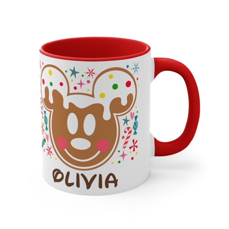 May include: White ceramic mug with a red interior and handle. The mug features a gingerbread Mickey Mouse design with the name "OLIVIA" in brown text. Colorful candy and star accents surround the character.