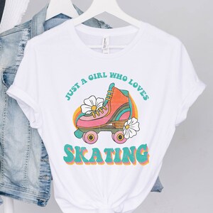 May include: White t-shirt with a retro graphic design featuring a roller skate with flowers and the text "Just a girl who loves skating".