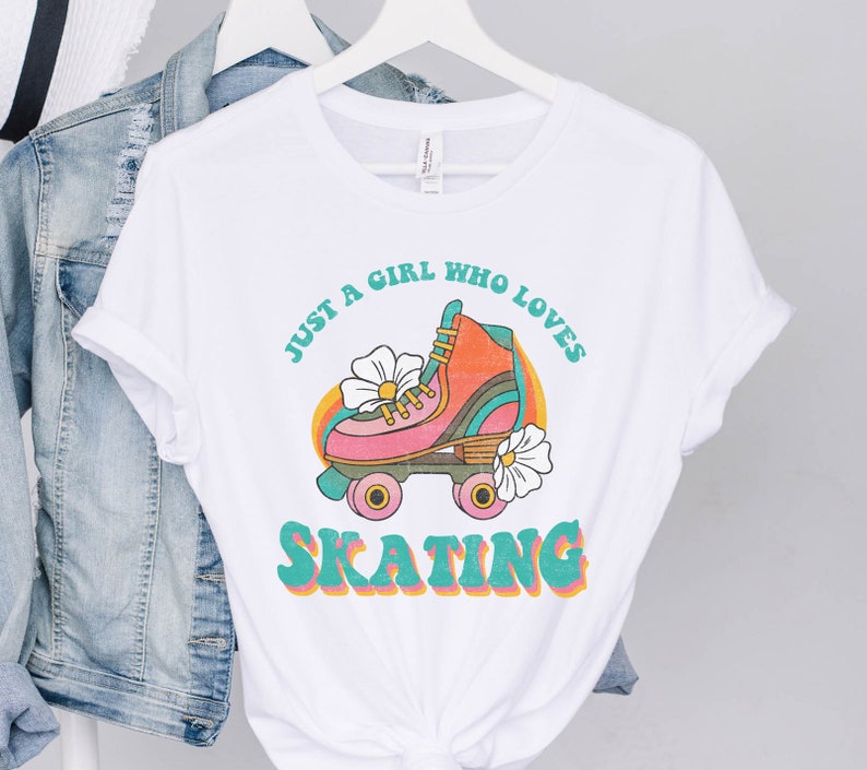May include: White t-shirt with a retro graphic design featuring a roller skate with flowers and the text "Just a girl who loves skating".