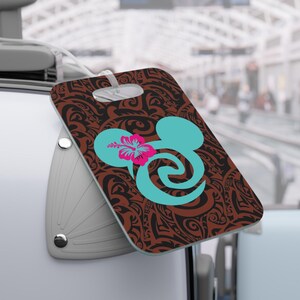 May include: A brown luggage tag with a black and brown tribal pattern. A turquoise Mickey Mouse head with a pink hibiscus flower is in the center of the tag.