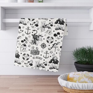 May include: Black and white kitchen towel with a repeating pattern of Mickey Mouse characters, anchors, and nautical themed illustrations. The text "All Aboard!" appears twice on the towel.