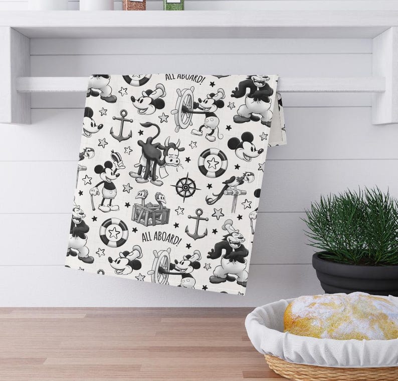May include: Black and white kitchen towel with a repeating pattern of Mickey Mouse characters, anchors, and nautical themed illustrations. The text "All Aboard!" appears twice on the towel.