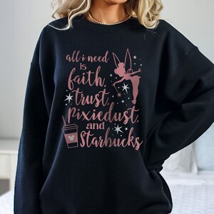 Op de afbeelding: Zwart sweatshirt met een roségouden opdruk. De afbeelding bevat de tekst "all I need is faith, trust, Pixiedust, and Starbucks", een feeënsilhouet en een Starbucks-beker met een Mickey Mouse-hoofd.