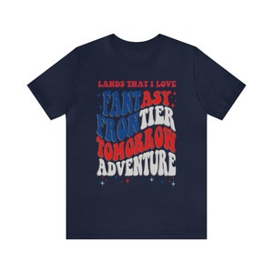 May include: Navy blue t-shirt with a retro-style graphic design. The text reads "Lands That I Love" and features the words "Fantasy", "Frontier", "Tomorrow", and "Adventure" in a wavy, layered design with red, white, and blue colors.