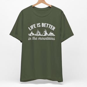 May include: A green t-shirt with the text "Life is better in the mountains" and a graphic of mountain peaks.