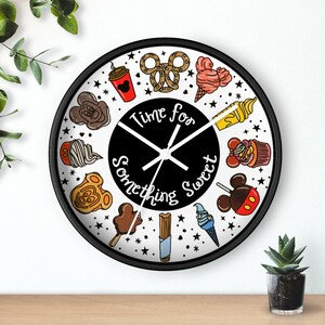 May include: A black and white round clock with a black frame. The clock face features a white background with black text that reads "Time for Something Sweet". The clock is decorated with various cartoon images of Disney-themed treats, including Mickey Mouse ears, ice cream cones, pretzels, and cupcakes.