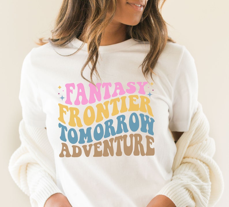 May include: White t-shirt with a retro-style graphic that reads "Fantasy Frontier Tomorrow Adventure" in pink, yellow, blue, and brown.
