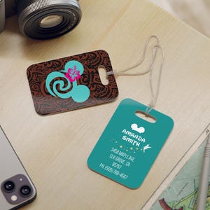 May include: Two luggage tags with a teal background and white Mickey Mouse ears. One tag has a brown and teal design with a pink flower and a swirl. The other tag has the text "AMANDA SMITH", "3458 MAPLE AVE", "ELK GROVE, CA", "95757", and "PH. (509) 788-4567".