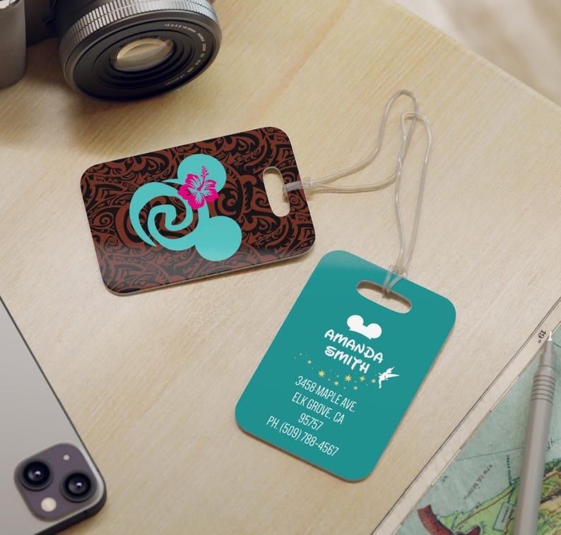 May include: Two luggage tags with a teal background and white Mickey Mouse ears. One tag has a brown and teal design with a pink flower and a swirl. The other tag has the text "AMANDA SMITH", "3458 MAPLE AVE", "ELK GROVE, CA", "95757", and "PH. (509) 788-4567".