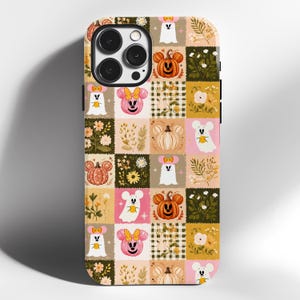 May include: A phone case featuring a patchwork pattern of autumn-themed squares. The design includes illustrations of ghosts with mouse ears, pumpkins with mouse ears, floral arrangements, and checkered prints in shades of orange, pink, and green.