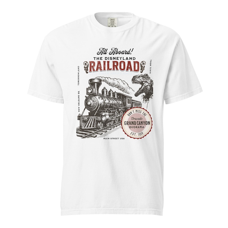May include: White t-shirt featuring a vintage illustration of a steam train with the text "All Aboard! The Disneyland Railroad." A dinosaur graphic is also included. The design is in black and red.