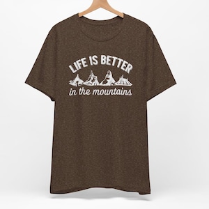 May include: A brown t-shirt with the text "Life is better in the mountains" and a graphic of mountain peaks.