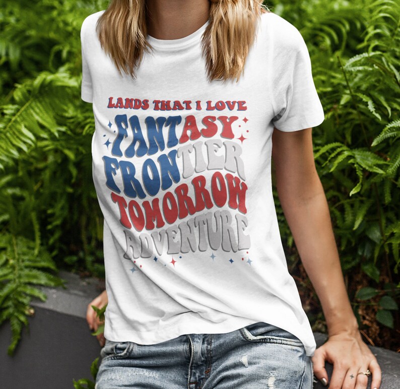 May include: White t-shirt with a red, white, and blue graphic that says "Lands That I Love: Fantasy Frontier Tomorrow Adventure".