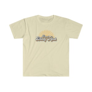May include: A light beige t-shirt with a retro-style graphic that says "Proud Disney Adult" with a sunburst behind the text. The text is in a blue, orange, and yellow color scheme.