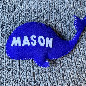May include: A blue felt whale with the name "MASON" embroidered in white felt.