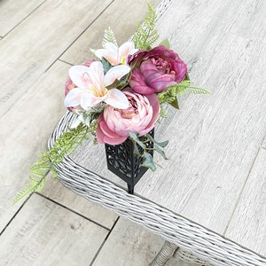 May include: A bouquet of pink and white flowers in a black metal vase. The flowers are arranged in a decorative way and the vase has a geometric design.