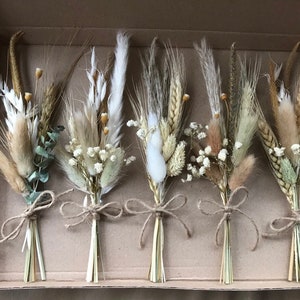 May include: Six small bouquets of dried flowers in a cardboard box. Each bouquet is tied with twine and features a mix of white, beige, and brown dried grasses and flowers.