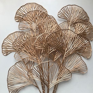 Könnte beinhalten: Ein Bund goldfarbener Ginkgoblätter aus Metall. Die Blätter sind fächerförmig angeordnet und haben eine zarte, drahtartige Struktur.