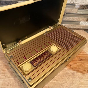 K&ouml;nnte beinhalten: Vintage Emerson-Radio mit cremefarbenem Geh&auml;use und goldfarbener Frontplatte. Das Radio hat eine rechteckige Form mit einem Klappdeckel. Die Frontplatte zeigt das Emerson-Logo und ein Zifferblatt. Das Radio ist ge&ouml;ffnet und zeigt den Lautsprecher und die internen Komponenten.