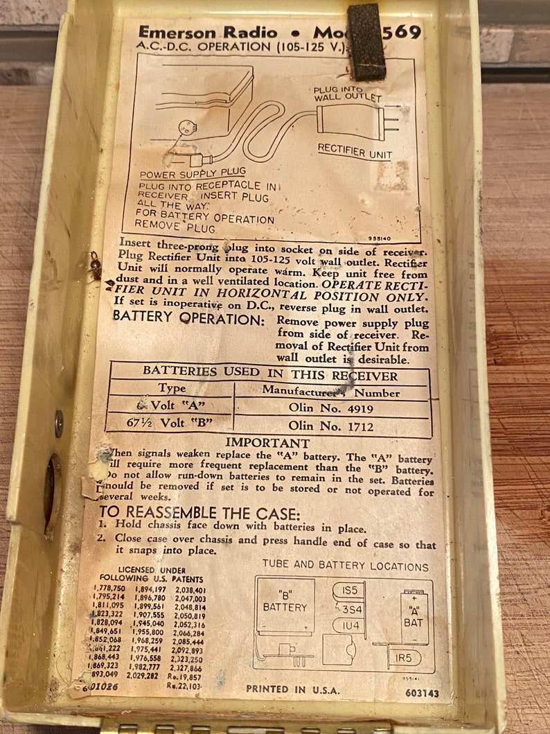 K&ouml;nnte beinhalten: Vintage Emerson Radio Modell 569 A.C.-D.C. Radiokomponenten. Das Innere des Radiogeh&auml;uses zeigt gedruckte Anweisungen, Diagramme sowie Batterie- und R&ouml;hrenstandorte. Das Geh&auml;use ist cremefarben.