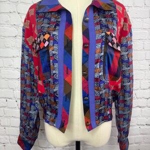 May include: A colourful, open jacket with a vibrant patchwork design. The jacket features a blue collar, purple trim, and a mix of red, blue, and patterned fabrics. It has long sleeves and button closures.