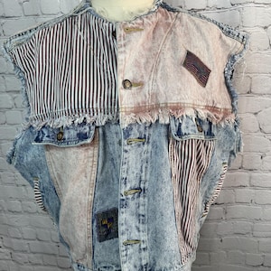 May include: A sleeveless denim vest with a patchwork design. The vest features sections of blue acid wash denim, pink fabric, and brown and white striped fabric. It has a frayed hem and several buttons.